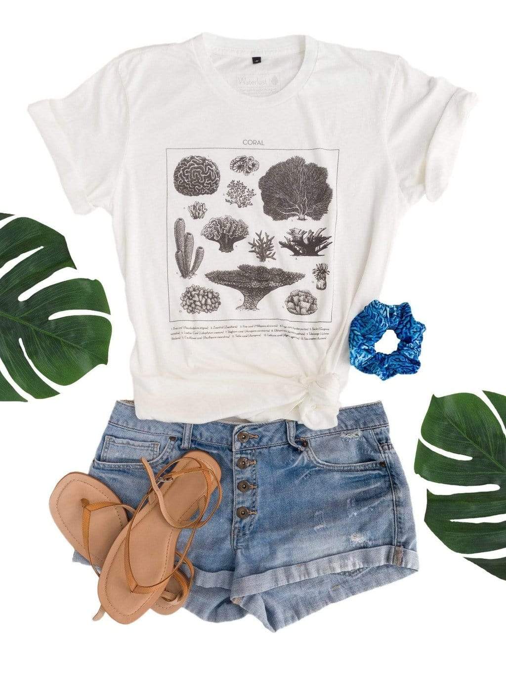 Styled view of the shirt flat with denim shorts, sandals, a scrunchie and monsterra leaves.