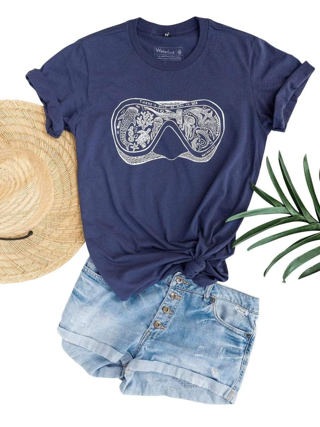 Waterlust &quot;There&#39;s Still So Much To Sea&quot; 100% Organic Cotton T Shirt - flat off body view styled with shorts, a sun hat and palm leaf